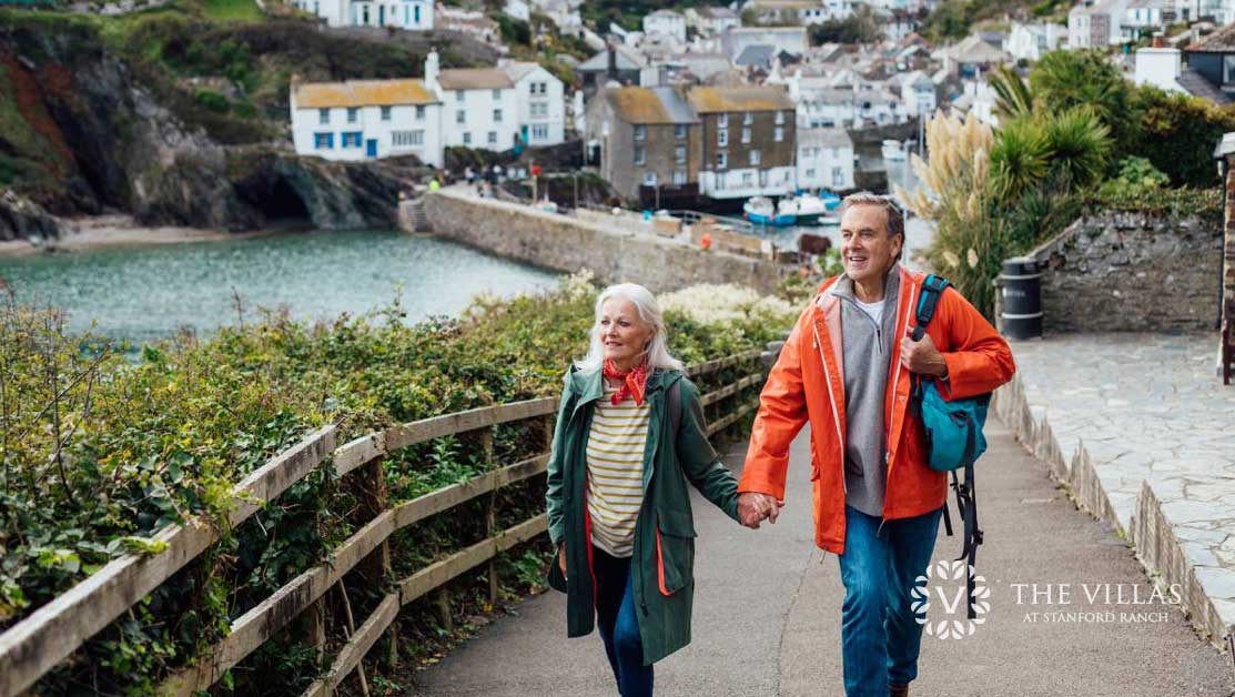 A senior couple walks along a path in a European seaside village.