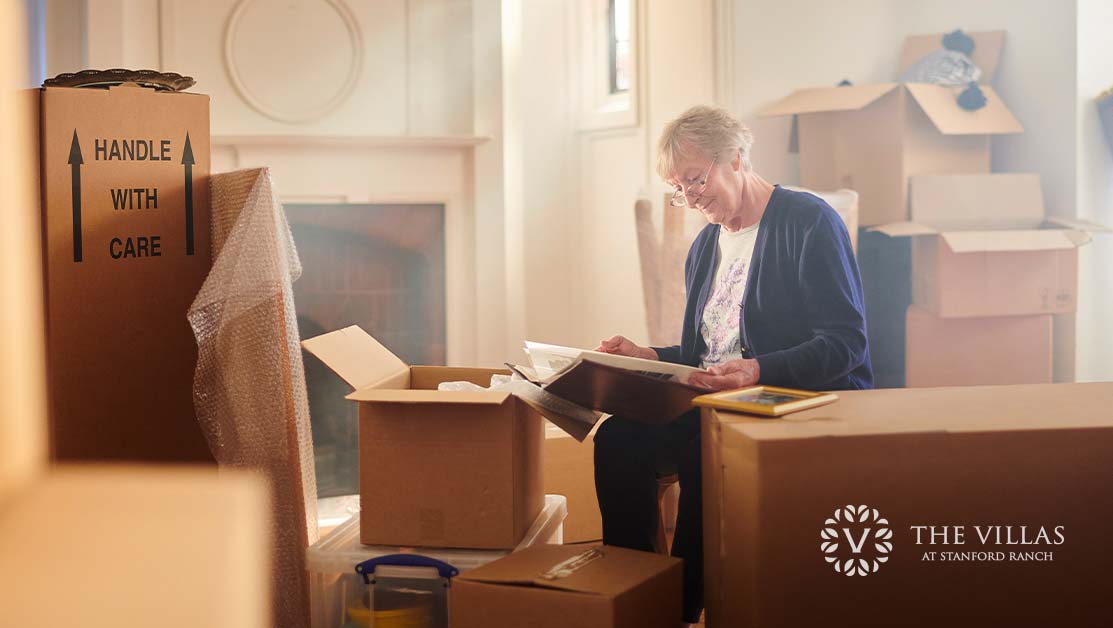 A senior woman packing to move reads a book surrounded by boxes.