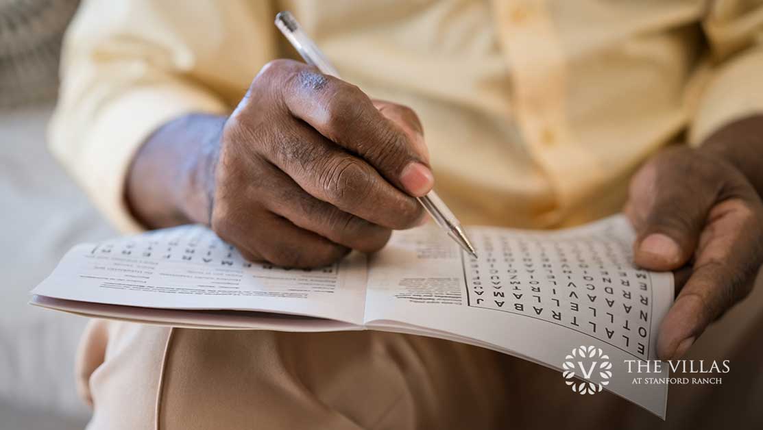 A senior holds a pen and does a crossword puzzle in a book.