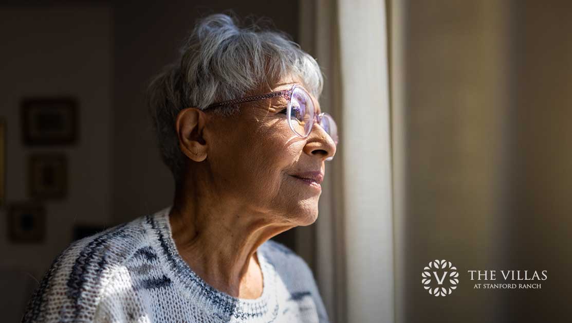 A senior woman is looking out the window of her home.