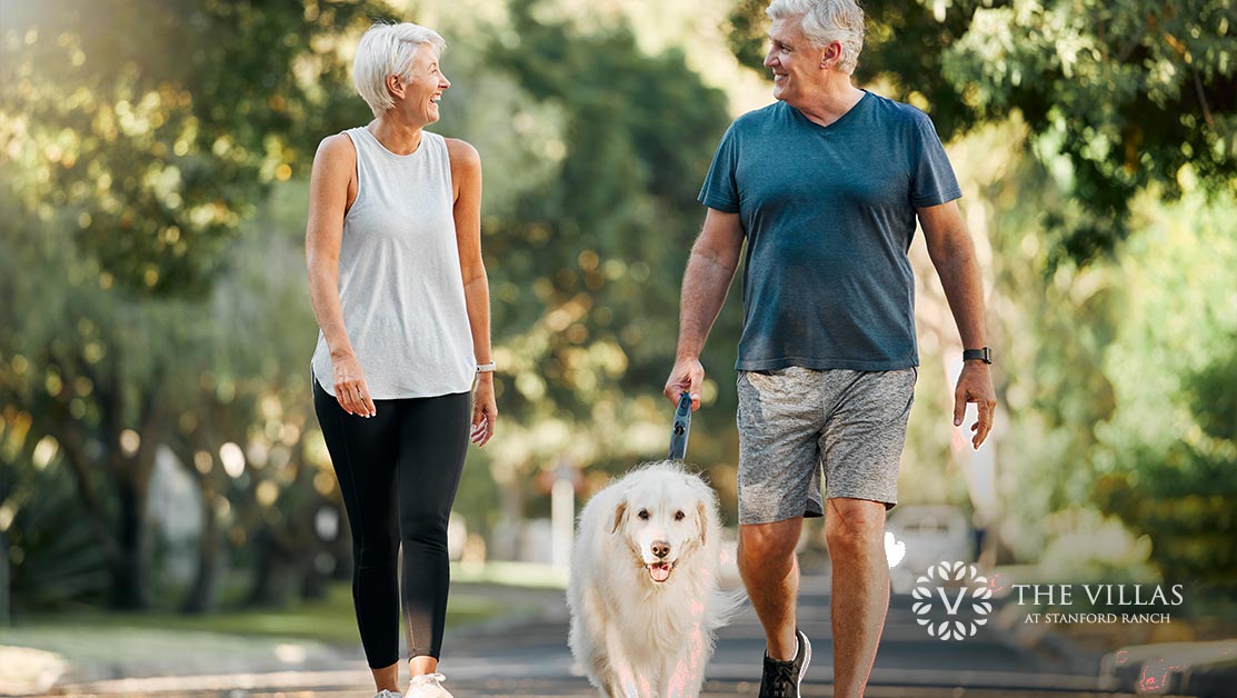 Senior couple walks outside with their dog on a nature trail. Discover 5 spring health tips for seniors.
