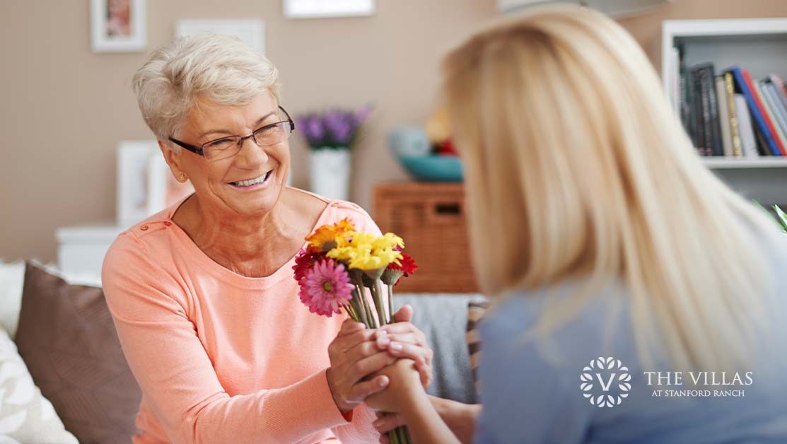 A senior woman is smiling as she receives a small bouquet of flower from her daughter. Discover Valentine's Day activities for seniors.