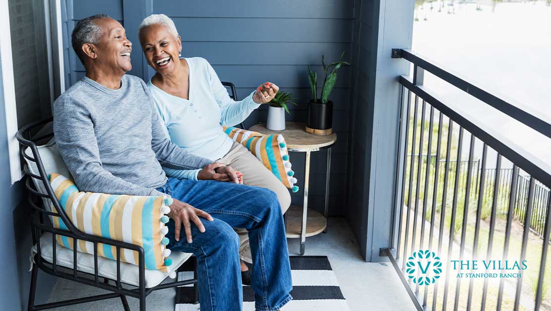 An elderly couple talking and laughing on their porch.