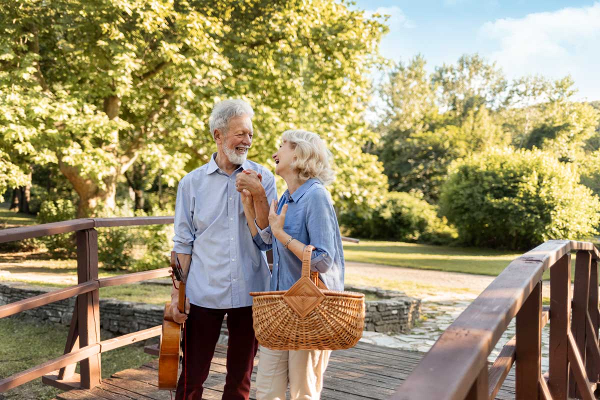 Older couple with gray hair laughing together and walking through a spring landscape.