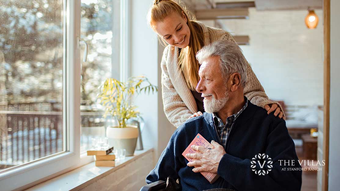 A young woman and an elderly man sitting by the window. Learn how to tell when it's time for assisted living.