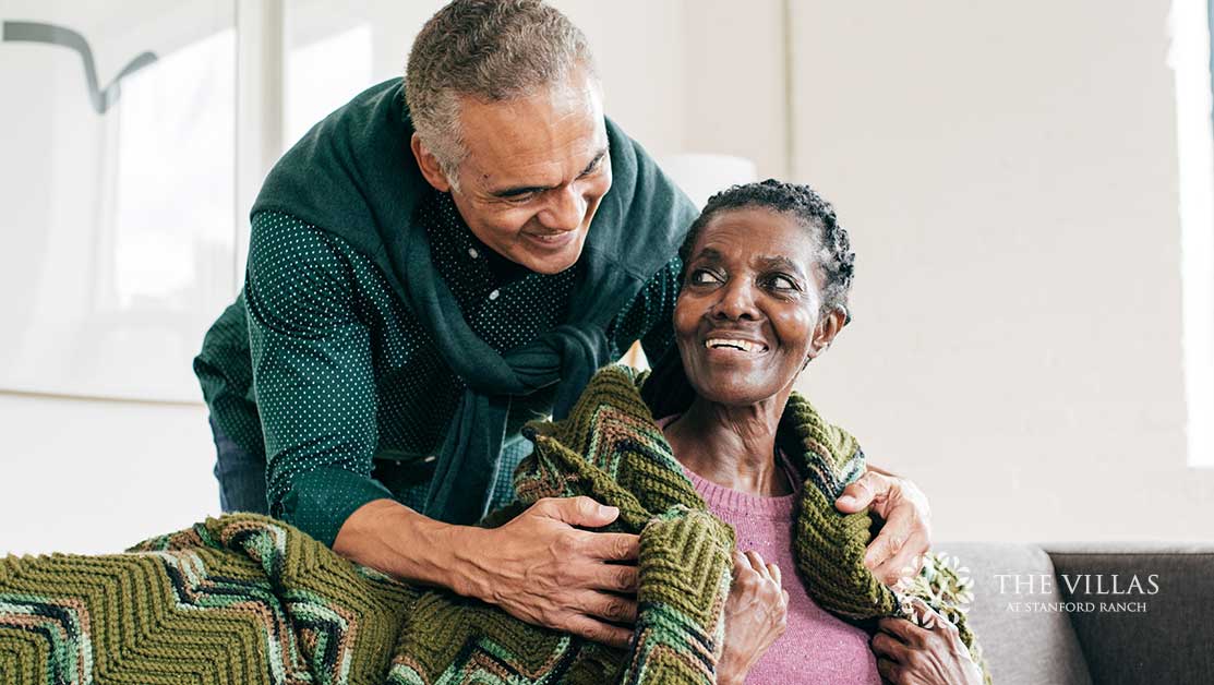 A man wraps an elderly woman’s shoulders in a blanket. Learn more about helping your loved one adjust to assisted living